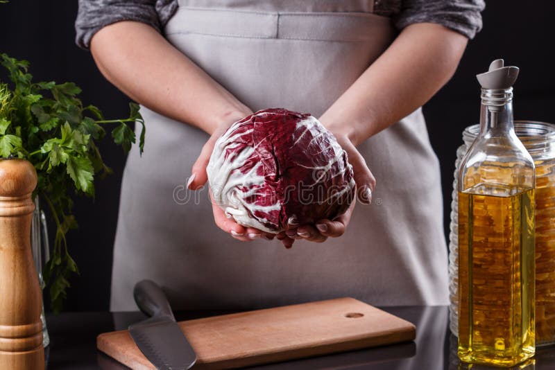 Ung kvinna i en grå aprons skär ner radicchio arkivfoto