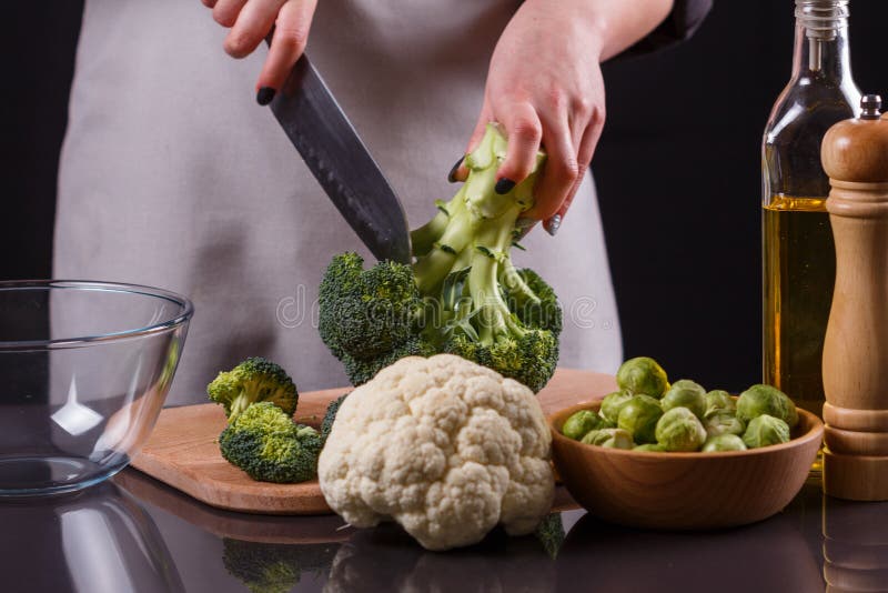 Ung kvinna i grå aproner skär blomkålbroccoli royaltyfria bilder