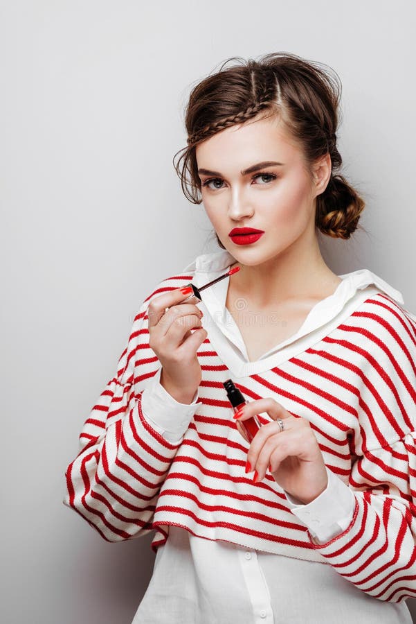 Ung kvinna med r?da kanter p? n?tt emotionell framsida i den eleganta kl?nningen som rymmer makeupl?ppstift i studio royaltyfri fotografi Ung kvinna med r?da kanter p? n?tt emotionell framsida i den eleganta kl?nningen som rymmer makeupl?ppstift i studio royaltyfri fotografi