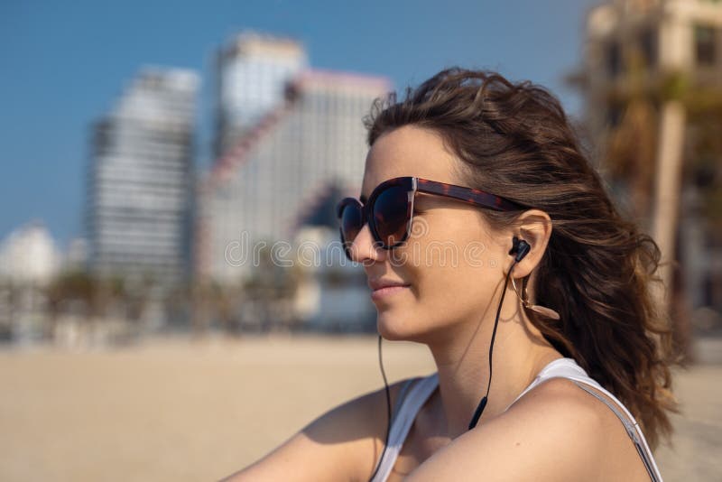 Ung kvinna p? den lyssnande musiken f?r strand med h?rlurar stadshorisont som bakgrund royaltyfri foto Ung kvinna p? den lyssnande musiken f?r strand med h?rlurar stadshorisont som bakgrund royaltyfri foto