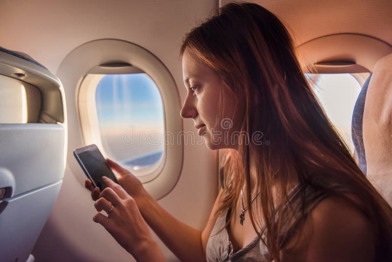 Ung kvinna som använder mobiltelefonen i flygplan på solnedgången arkivbilder Ung kvinna som använder mobiltelefonen i flygplan på solnedgången arkivbilder