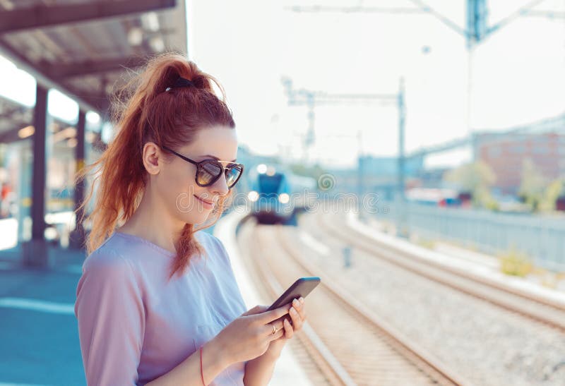 Ung kvinna som använder sin mobiltelefon på tunnelbaneplattform, kontrollerar meddelanden via sms-mail eller tågschema