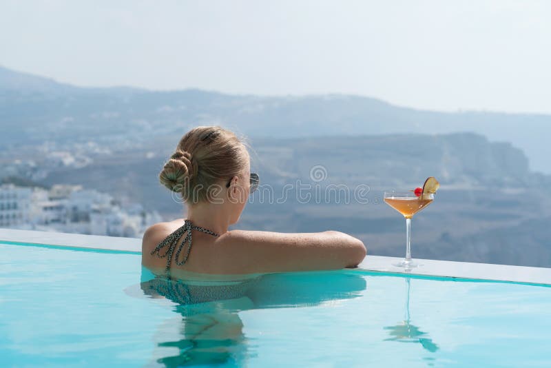 Ung kvinna som kopplar av i pölen med en ursnygg sikt på Santorini arkivbild Ung kvinna som kopplar av i pölen med en ursnygg sikt på Santorini arkivbild