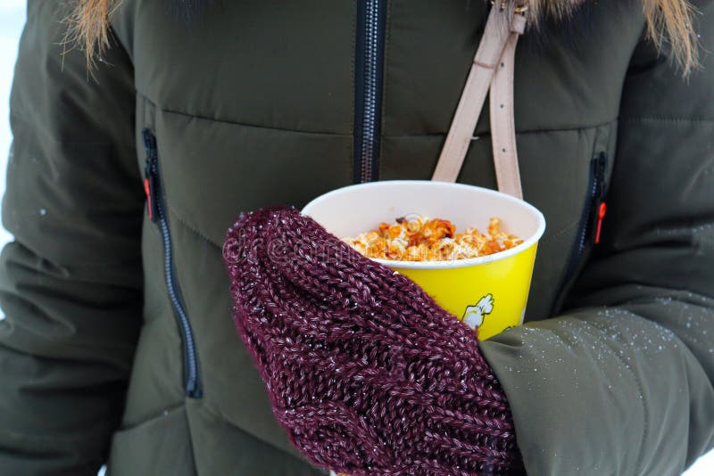 Ung kvinna som rymmer popcorn i vinter, i tumvanten arkivfoton Ung kvinna som rymmer popcorn i vinter, i tumvanten arkivfoton