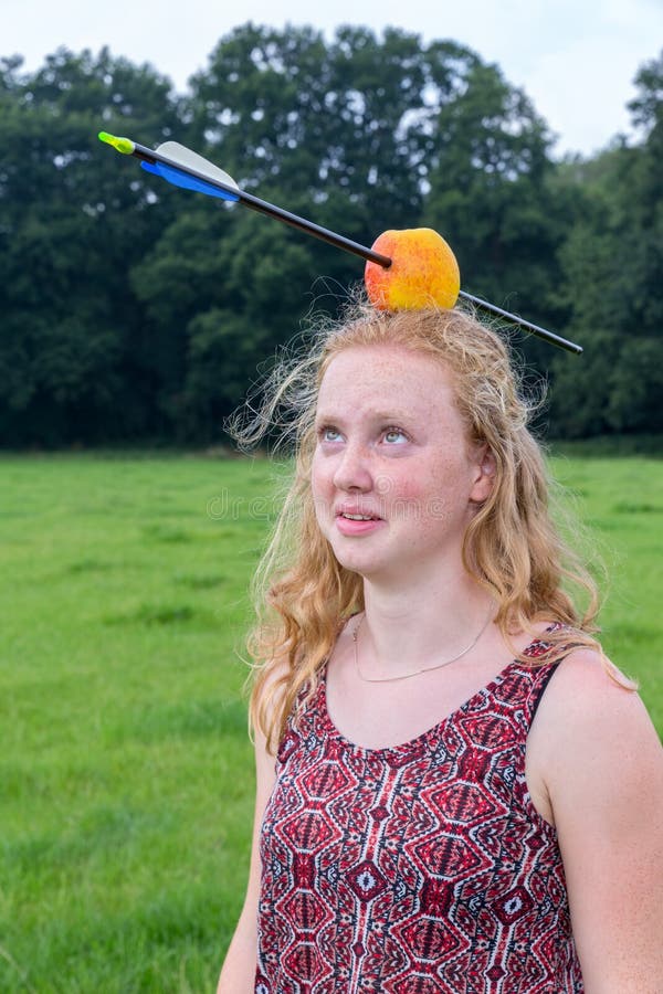 Young woman looking afraid at arrow in apple on head outdoors. Young woman looking afraid at arrow in apple on head outdoors