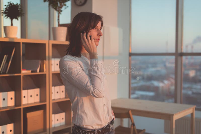 Ung kvinna som talar genom att använda mobiltelefonen på kontoret i aftonen Koncentrerad kvinnlig affärskvinna och att se framåtr royaltyfri fotografi Ung kvinna som talar genom att använda mobiltelefonen på kontoret i aftonen Koncentrerad kvinnlig affärskvinna och att se framåtr royaltyfri fotografi
