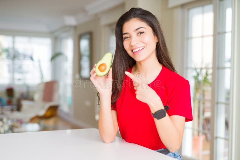 Ung kvinna som äter friska avocado och som är mycket glad över att peka med hand och finger arkivbild