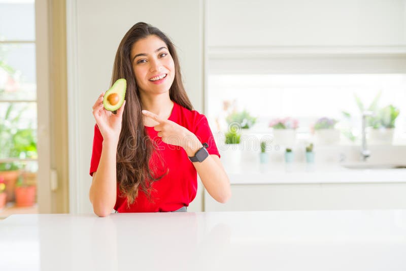 Ung kvinna som äter friska avocado och som är mycket glad över att peka med hand och finger royaltyfri foto