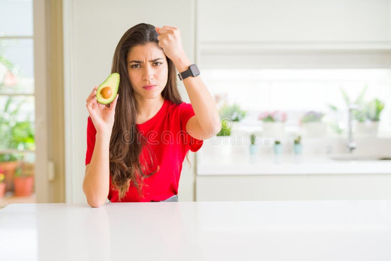 Ung kvinna som äter friska avokado irriterad och frustrerad skrik med ilska och skrik med upphöjda idéer om handvrede royaltyfri foto