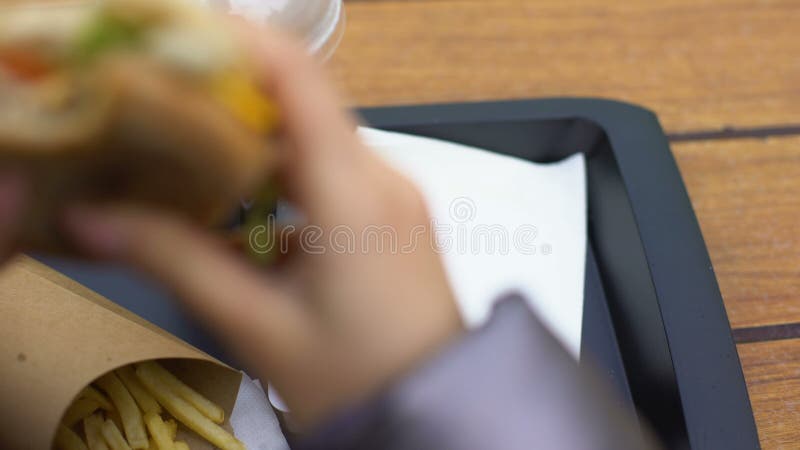 Ung kvinna som äter hamburgaren och att ha lunch i snabbmatrestaurang, viktförlust