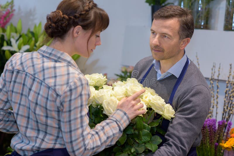 Ung kvinnlig väljande höger blomma för manlig blomsterhandlareportion royaltyfri foto Ung kvinnlig väljande höger blomma för manlig blomsterhandlareportion royaltyfri foto
