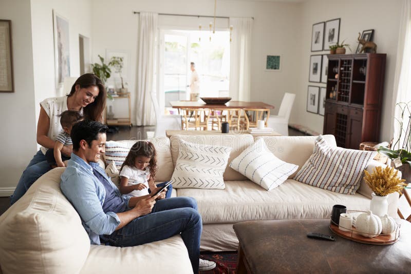 Ung latinamerikansk familj som sitter på soffan som tillsammans läser en bok i deras vardagsrum