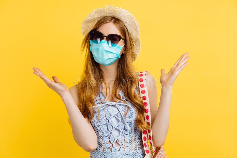 Ung, lycklig kvinna i medicinskt skyddsmask och sommarhatt i sommarkläder på gul bakgrund arkivbild
