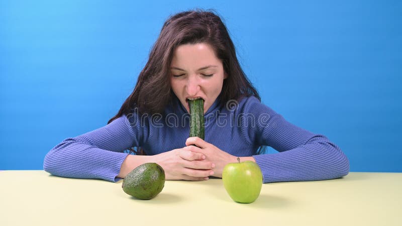 Ung lycklig kvinna som äter stor gurka på blå bakgrund. begreppet vegetarianism arkivbild