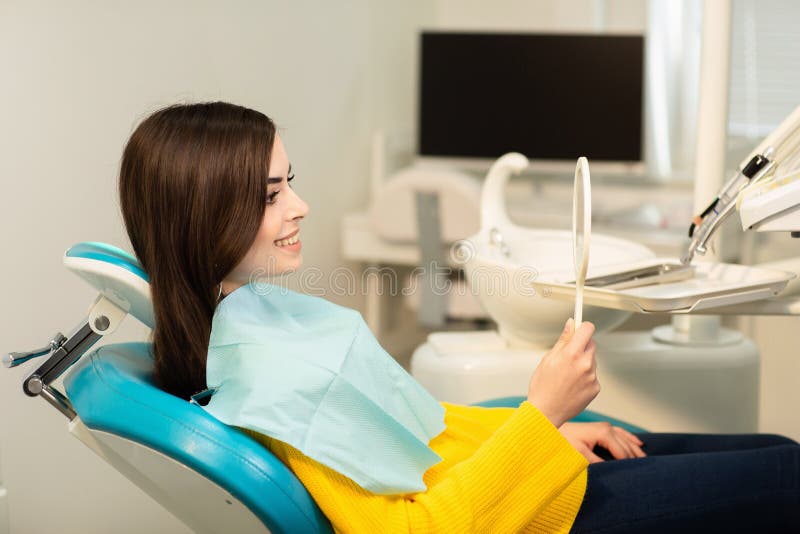 Ung lycklig kvinnaklient som ser spegeln med toothy leende p? det tand- kontoret arkivbilder Ung lycklig kvinnaklient som ser spegeln med toothy leende p? det tand- kontoret arkivbilder