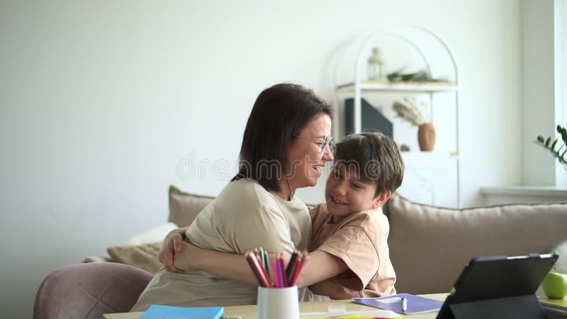 Ung mamma son kramar och sitter vid bordet med en tablett i lägenhetsrummen.. arkivfilmer