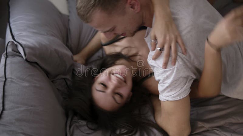 Ung man i den vita T-skjortan som kramar hans le långhåriga brunettflicka som ligger på henne Topview av gulliga unga par