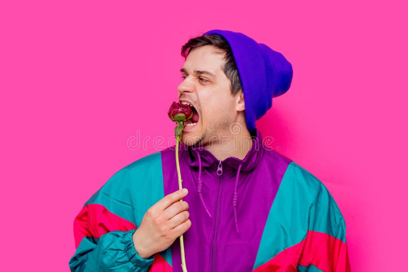 Ung man i 90-talkläder som äter blomningpionblomman royaltyfri bild Ung man i 90-talkläder som äter blomningpionblomman royaltyfri bild