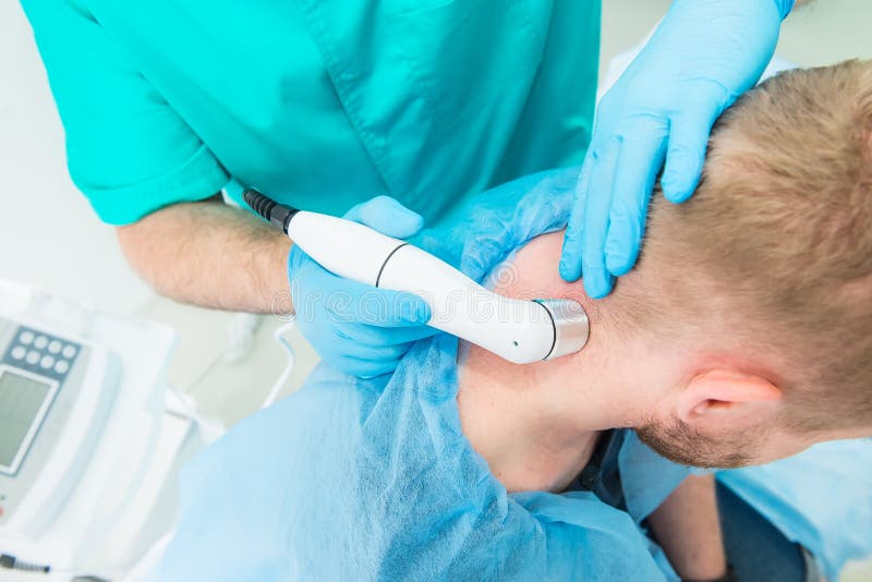 Ung man p? sjukgymnastiken som mottar laser-terapimassage En kiropraktor behandlar patientens cervikala rygg i medicinskt kontor fotografering för bildbyråer Ung man p? sjukgymnastiken som mottar laser-terapimassage En kiropraktor behandlar patientens cervikala rygg i medicinskt kontor fotografering för bildbyråer