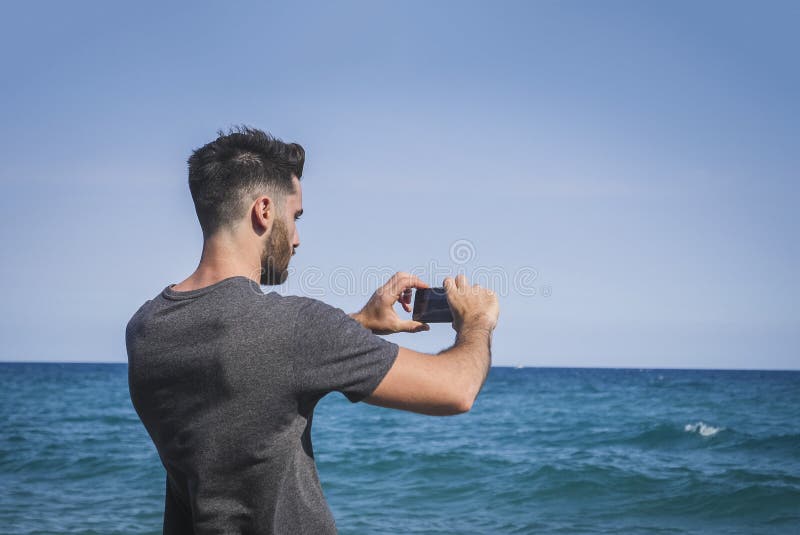 Ung man som använder mobiltelefonen för att ta fotoet på stranden royaltyfria bilder Ung man som använder mobiltelefonen för att ta fotoet på stranden royaltyfria bilder
