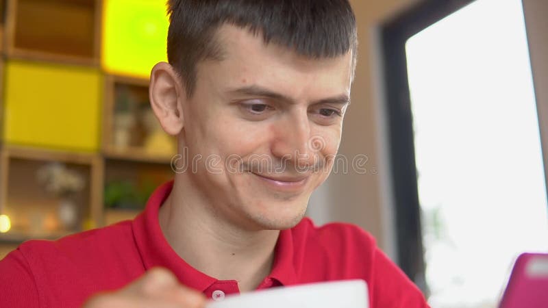 Ung man som dricker kaffe och överför meddelanden med hans mobiltelefon lager videofilmer