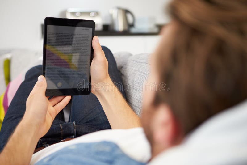 Young Man Relaxing On Sofa Using Digital Tablet At Home. Young Man Relaxing On Sofa Using Digital Tablet At Home