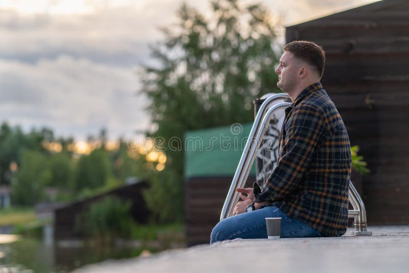 Ung man som sitter på en träbårgång vid solnedgången