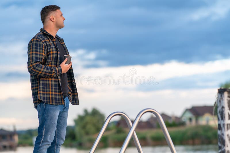 Ung man som står på en bardpromenad ovanför en sjö eller flod