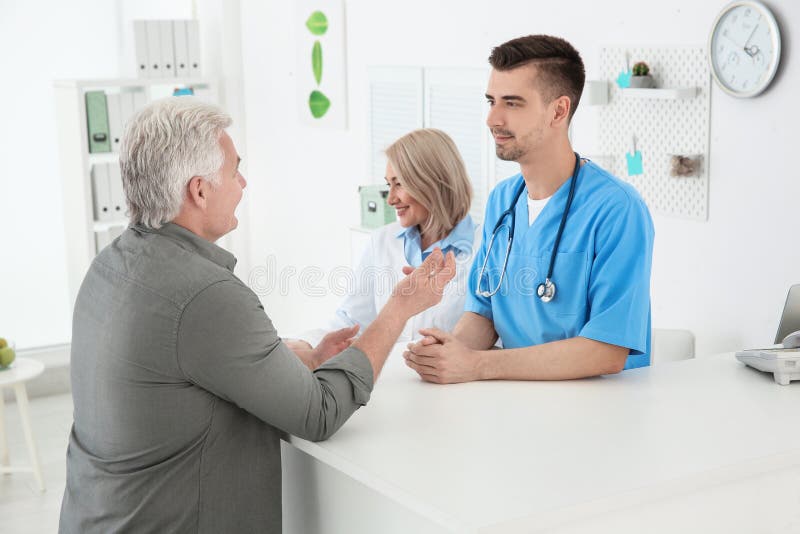 Ung manlig doktors- och pensionärkvinnligreceptionist arkivfoto Ung manlig doktors- och pensionärkvinnligreceptionist arkivfoto