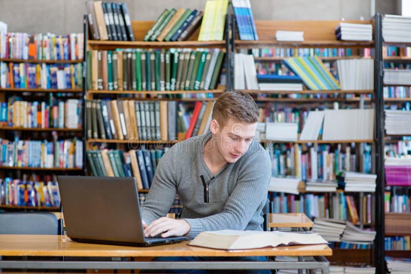 Ung maskinskrivning för manlig student på bärbara datorn i universitetarkivet royaltyfri foto Ung maskinskrivning för manlig student på bärbara datorn i universitetarkivet royaltyfri foto