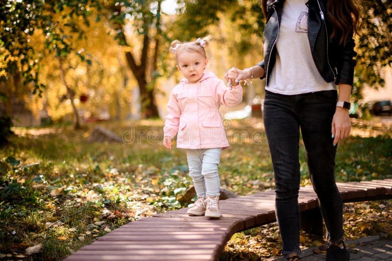 Ung mor som håller sin lilla dotter hand och hjälper till att gå på bänken royaltyfri bild Ung mor som håller sin lilla dotter hand och hjälper till att gå på bänken royaltyfri bild