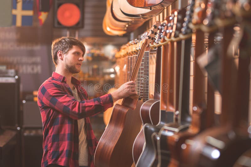 Ung musiker som väljer en gitarr i ett lager arkivfoton