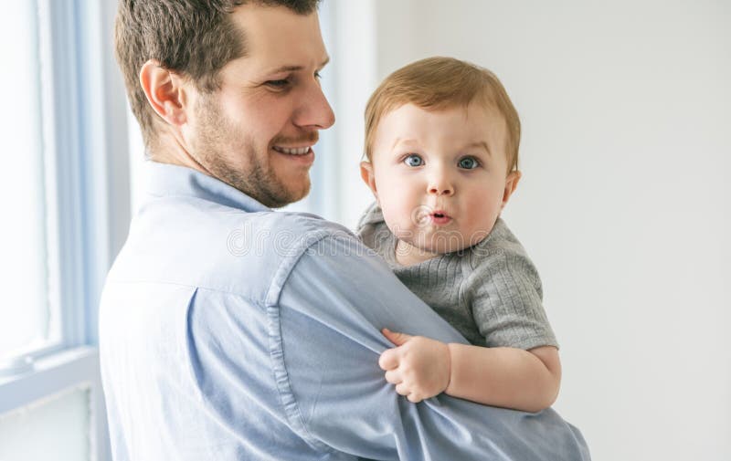 Ung pappa med en babypojke som hade kul med sin son nära ett fönster royaltyfria foton