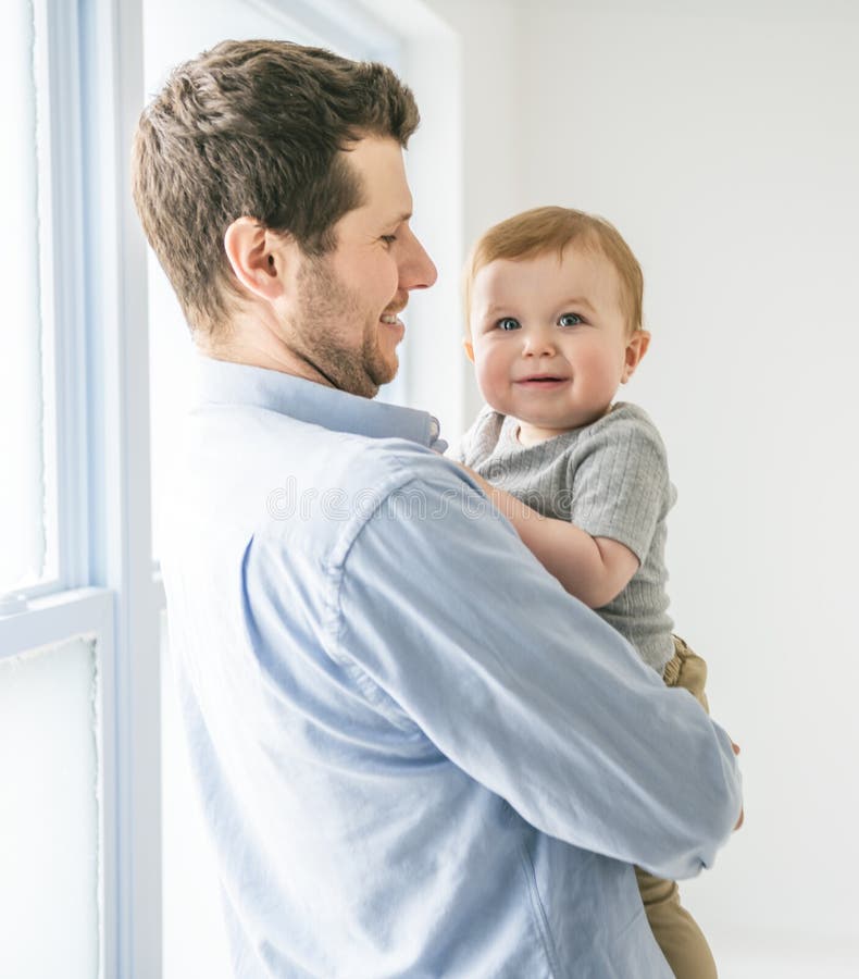 Ung pappa med en babypojke som hade kul med sin son nära ett fönster royaltyfri foto