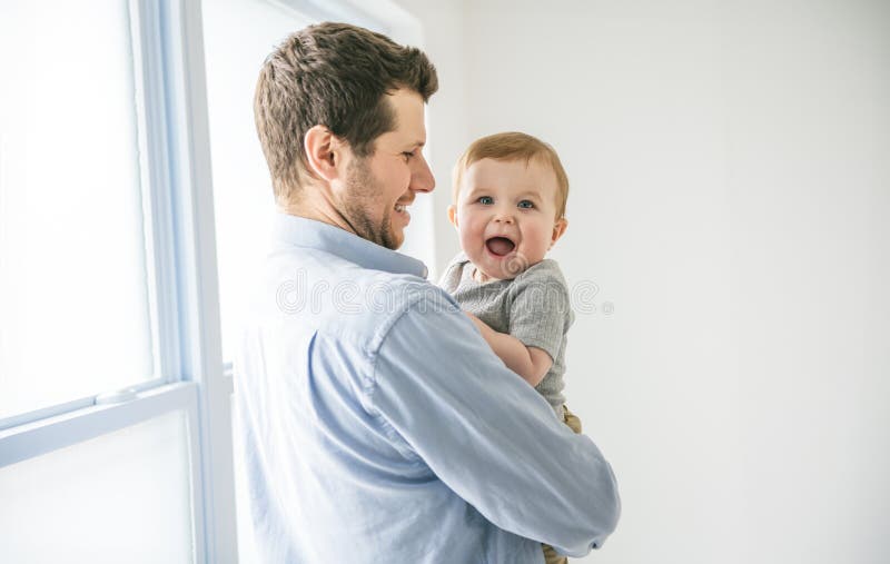 Ung pappa med en babypojke som hade kul med sin son nära ett fönster arkivbilder