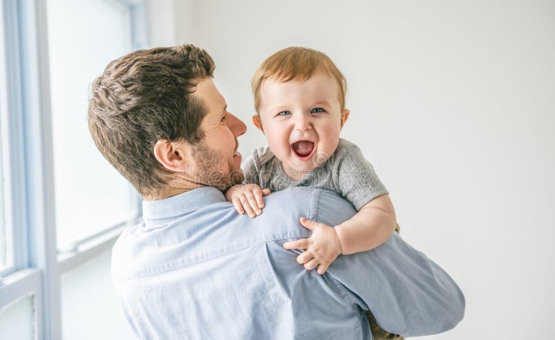 Ung pappa med en babypojke som hade kul med sin son nära ett fönster royaltyfria foton