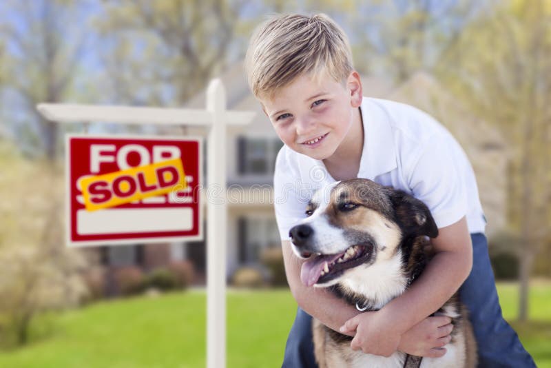 Ung pojke och hans hund framme av Sold det till salu tecknet och huset arkivbild Ung pojke och hans hund framme av Sold det till salu tecknet och huset arkivbild