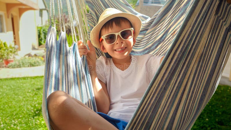 Ung pojke som bar en hatt som en blixtfull svällning i en hammock en verklig skildring av karefria semestervibes royaltyfri foto