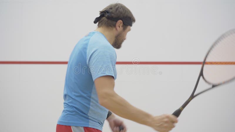 Ung positiv tränare som visar tummen upp till idrottsmannen som spelar squash på gymmet. porträtt av koncentrerad midvuxen skäggig