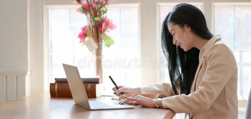 Ung professionell affärskvinna som arbetar med sitt projekt när hon skriver på en bärbar dator i ett bekvämt rum royaltyfria bilder