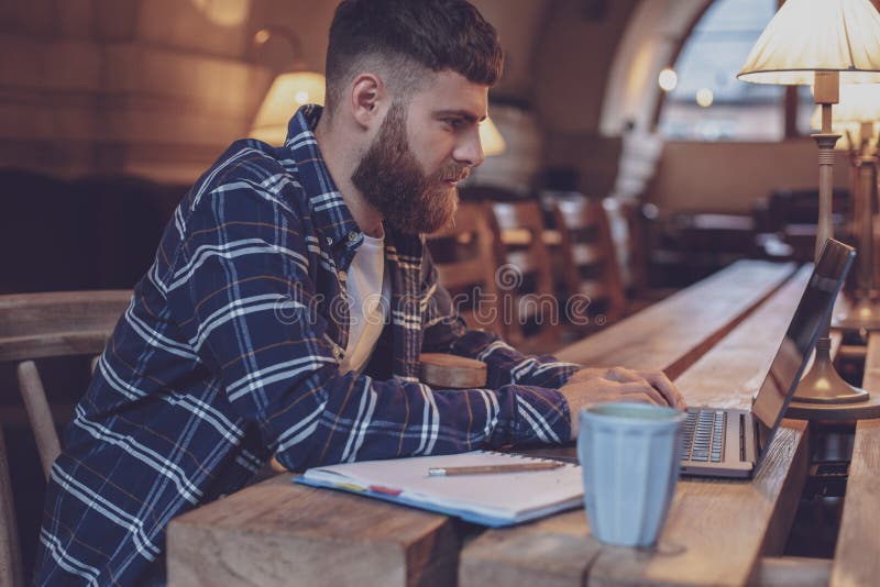 Ung professionell som surfar internet på hans bärbar dator i ett kafé arkivbild Ung professionell som surfar internet på hans bärbar dator i ett kafé arkivbild