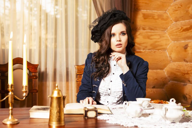 Ung, sensuell caucasian brunette-kvinna som pockar i retro-klädsel med kaffepott och syltläsbok vid bordet i byn royaltyfri foto