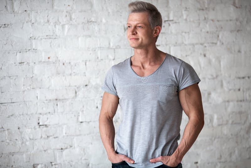 Ung sexig stående för studio för mankroppsbyggareidrottsman nen i vind på bakgrunden av den vita tegelstenväggen Stilig grabbmode royaltyfria bilder Ung sexig stående för studio för mankroppsbyggareidrottsman nen i vind på bakgrunden av den vita tegelstenväggen Stilig grabbmode royaltyfria bilder