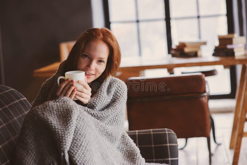 Ung sjuk kvinna som läker med den varma drinken som är hemmastadd på den hemtrevliga soffan arkivbild Ung sjuk kvinna som läker med den varma drinken som är hemmastadd på den hemtrevliga soffan arkivbild
