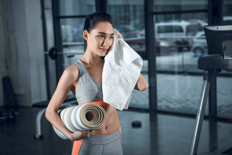 ung sportig kvinna med rullande matt avtorking för yoga som svettas med handduken efter övningar