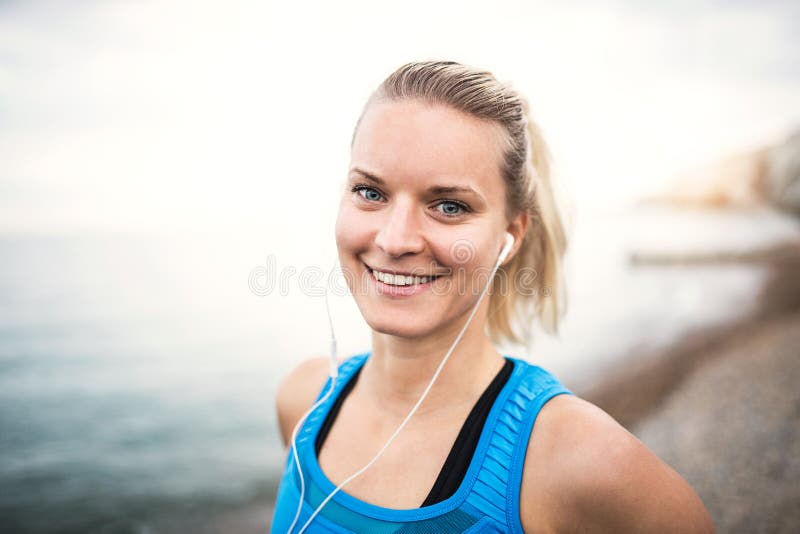 Ung sportig kvinnalöpare med hörlurar som utanför står på stranden arkivbilder Ung sportig kvinnalöpare med hörlurar som utanför står på stranden arkivbilder