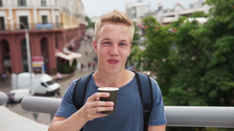 Ung stilig blond man som dricker kaffe och ler på den stads- gatan arkivfilmer