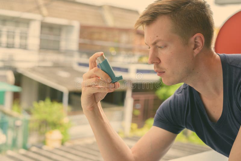 Ung, stilig man som använder astmamininhalator hemma royaltyfria bilder
