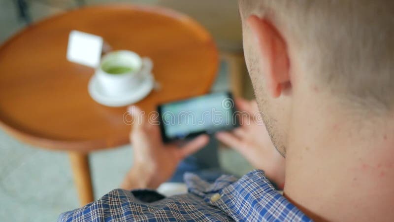 Ung stilig man som dricker Matcha grönt te och håller ögonen på videoen på mobiltelefonen i kafét Slowmotion livsstil för HD lager videofilmer