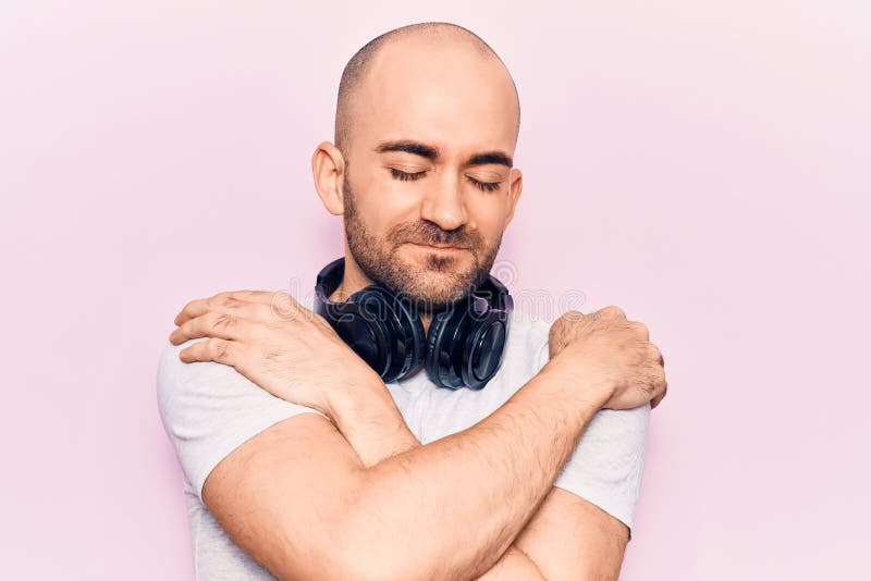 Ung, stilig man som lyssnar på musik med hörlurar som kramar sig själv, glad och positiv, leende självsäker royaltyfria foton